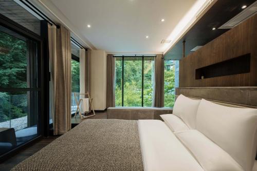 a bedroom with a white bed and large windows at 青城山坐忘森林疗愈酒店 in Dujiangyan