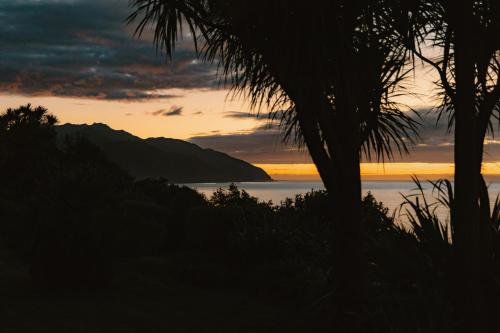 a sunset over the ocean with a palm tree at Oceanview Suite in Hapuku
