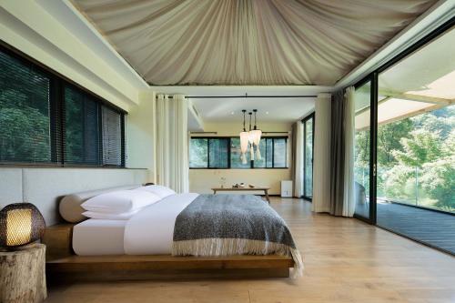 a bedroom with a bed and large windows at 青城山坐忘森林疗愈酒店 in Dujiangyan
