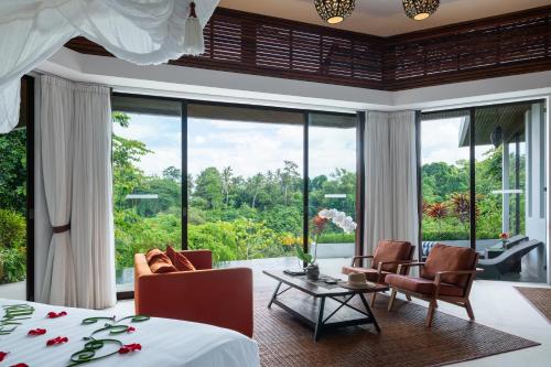 a bedroom with a bed and chairs and a large window at Cahaya Indah Villas in Ubud