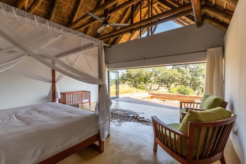 HectorspruitにあるLuxury & Wildlife Mlambo Lodge Mjejaneのベッドと椅子2脚と窓のある寝室