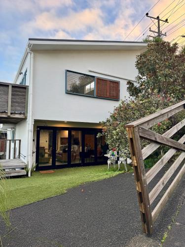 a white house with a wooden fence in front of it at Sandy Toes & Netflix Nights, Relaxing Auckland Retreat in Auckland