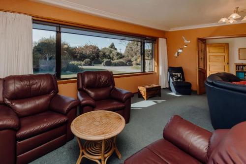 a living room with leather furniture and a large window at Mt Taranaki Vista - rural escape with scenic views in Okaiawa