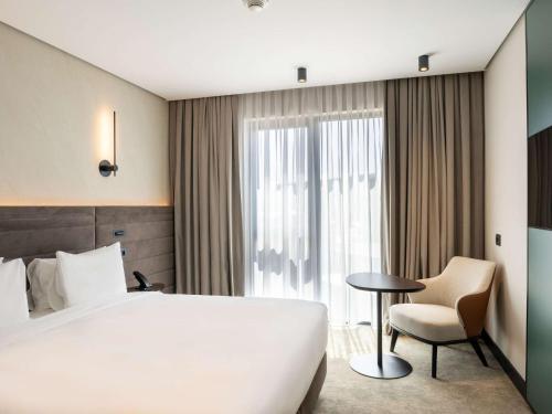 a hotel room with a large white bed and a chair at Novotel Tbilisi Center in Tbilisi City