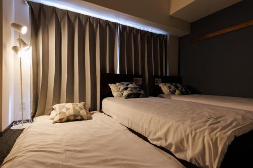a bedroom with two beds and a window with curtains at Grande Famille Shimanouchi Dotonbori Condo in Osaka