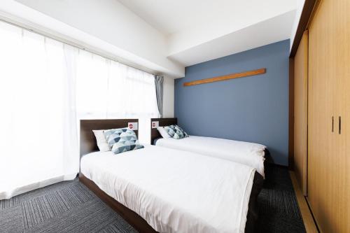 two beds in a bedroom with a blue wall at Grande Famille Shimanouchi Dotonbori Condo in Osaka