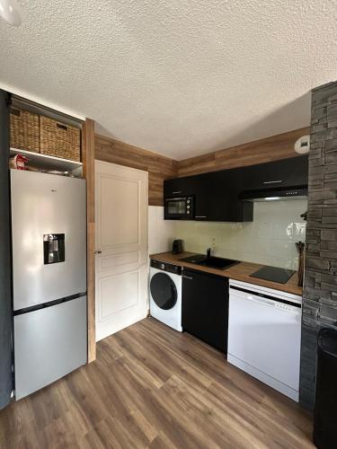 La cuisine est équipée d'un réfrigérateur blanc et d'un lave-vaisselle. dans l'établissement Appartement rénové au pied des pistes avec piscine, sauna, linge inclus et animaux acceptés, à Flumet