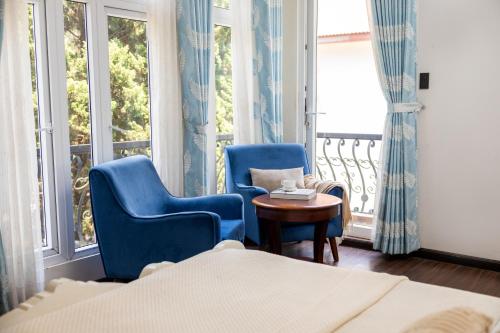 a room with two blue chairs and a table and windows at TTR Joy Apart' Hotel in Da Lat