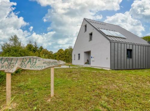 a white barn with a sign in front of it at Holiday Home Mali Raj in Ogulin