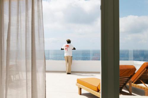 a man looking out a window at the ocean at Caramelo Marina Calan Bosch - Adults Only in Cala en Bosc