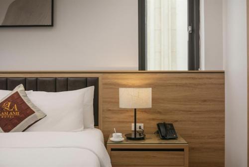 a bed with a lamp and a phone on a night stand at Lam Anh Hotel 5 Him Lam Vạn Phúc in Hà Ðông