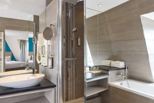 une salle de bain avec un lavabo, une baignoire et un miroir dans l'établissement Timhotel Montmartre, à Paris