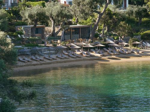 a beach with chairs and umbrellas next to the water at Grecotel Eva Palace in Kommeno