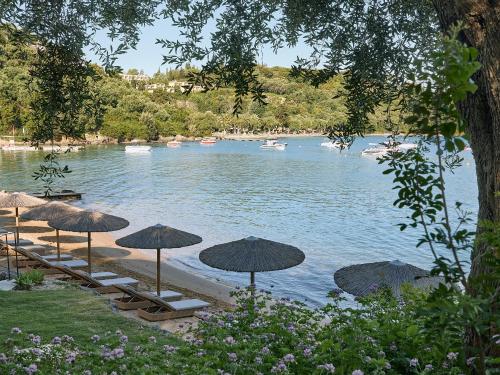 a beach with umbrellas and chairs and a body of water at Grecotel Eva Palace in Kommeno