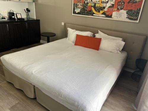 a large white bed with an orange pillow on it at Adagio Nice Centre in Nice