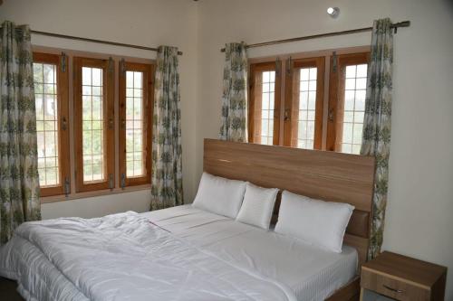 Schlafzimmer mit einem weißen Bett und Fenstern in der Unterkunft Negi Hotel in Mukteswar