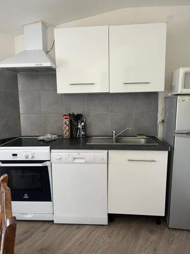 a kitchen with white cabinets and a sink and a refrigerator at Gîte meublé in Pont-Trambouze