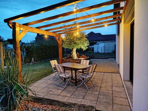 un patio avec une table et des chaises sous une pergola en bois dans l'établissement Maison récente avec jardin., à Plourhan
