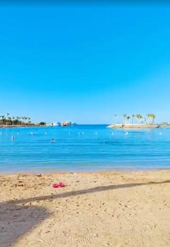 a sandy beach with blue water and an island in the distance at Hurghada Mirage Bay Hotel & Aquapark in Hurghada