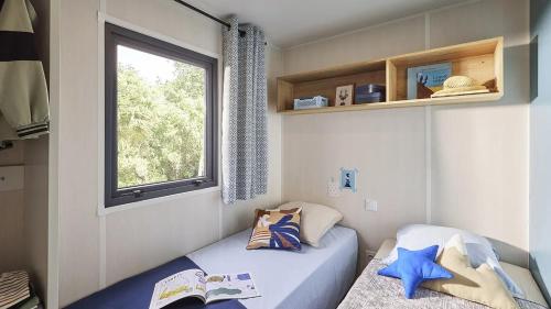 une petite chambre avec deux lits et une fenêtre dans l'établissement Kokua Vacances présente MOBIL HOME résidentiel toutes options camping 3 étoiles LESCAR, à Lescar