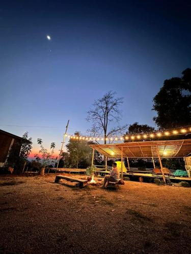 a man sitting at a picnic table under a tent with lights at Doichang Riverhouse in Ban Huai Khai