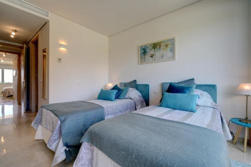 two beds in a white room with blue pillows at Ribera del Marlin IX Sotogrande in Sotogrande