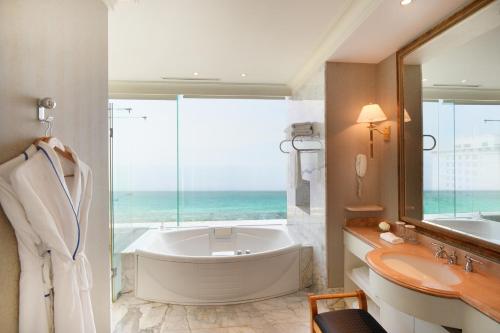 baño con bañera, lavabo y ventana en Jeju Oriental Hotel & Casino en Jeju