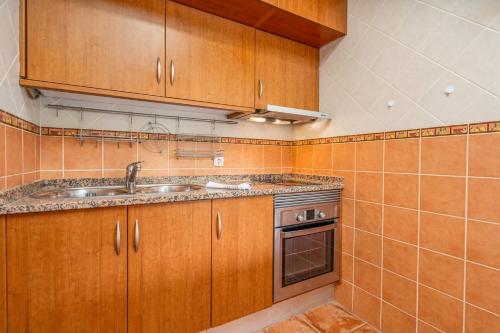 a kitchen with wooden cabinets and a sink and a stove at HostWise - Sunny Flat Near Praia da Rocha in Portimão