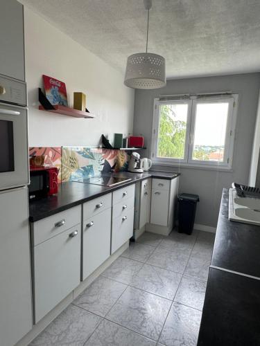 une cuisine avec des armoires blanches et un comptoir noir dans l'établissement Logement lumineux pour 6 personnes, à La Roche-sur-Yon