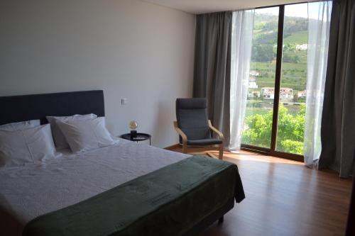 a bedroom with a bed and a chair and a window at Quinta do Santo no Douro - Casa T2 in Alcarias