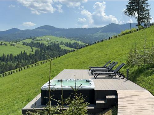 a deck with a hot tub and chairs on a hill at Vershe in Verkhovyna