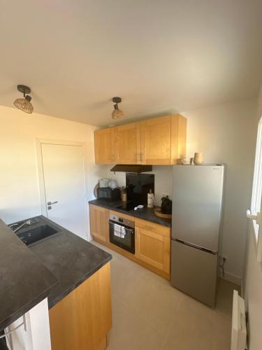une cuisine avec des armoires en bois et un réfrigérateur en acier inoxydable dans l'établissement Maison cosy à 10 minutes de la plage, à Gujan-Mestras