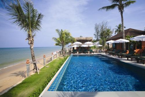 a swimming pool next to a beach with umbrellas at The Shambhala Khaolak Resort in Khao Lak