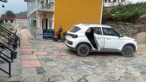 a white car parked next to a building with a scooter at Shivalik Dharohar ,barkot in Sar