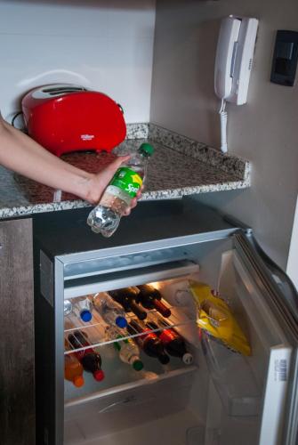 a person holding a bottle of water in an open refrigerator at Links Apart Hotel in Río Grande