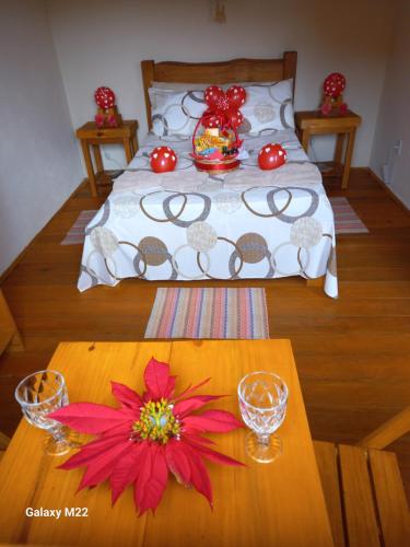 a bed with a table with red flowers on it at Cabana refúgio do tico tico 07 in Cunha