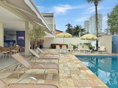 a pool with chairs and tables and umbrellas at Suíte Piscina e Churrasqueira AC Acesso a Praia in Guarujá