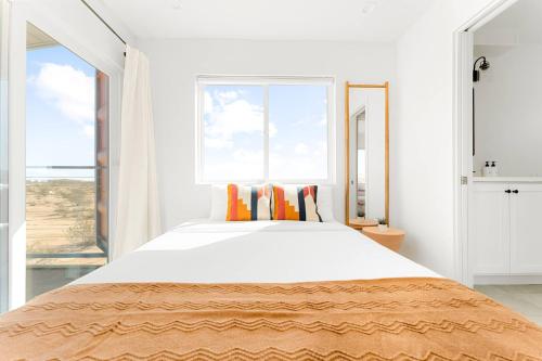 a white bedroom with a large bed with orange pillows at 3-Story Container Home | Pool • Spa • Rooftop Deck in Hidden River