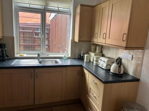 a kitchen with wooden cabinets and a sink and a window at Entire 2-Bedroom House Dudley in Sedgley