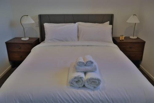 two towels on a bed with two night stands at Cosy 2BR House in Awaroa Road in Auckland