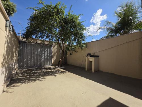 a fence with a tree in front of a wall at Suíte1 Privativa Climatizada Mobiliada com Garagem e Wi-Fi in Goiânia