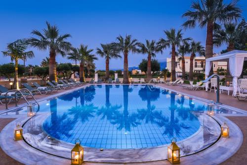a large swimming pool with palm trees and lights at Ammos Boutique Apartments & Suites in Malia