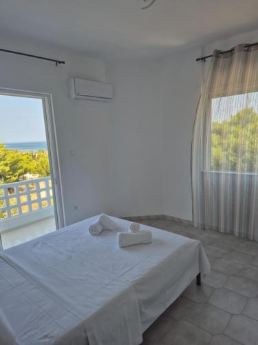 a white bedroom with a bed and a large window at Deco Apartments Aigina in Vaia