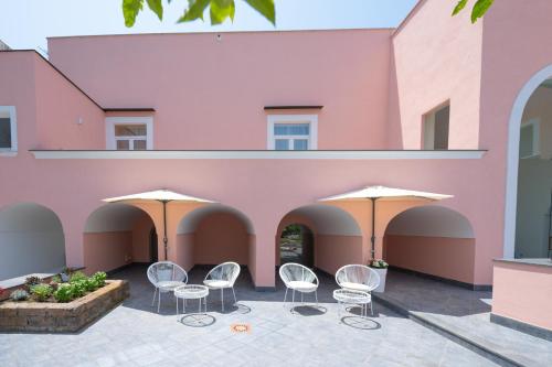 a pink building with white chairs and umbrellas at Aria Rooms in Procida