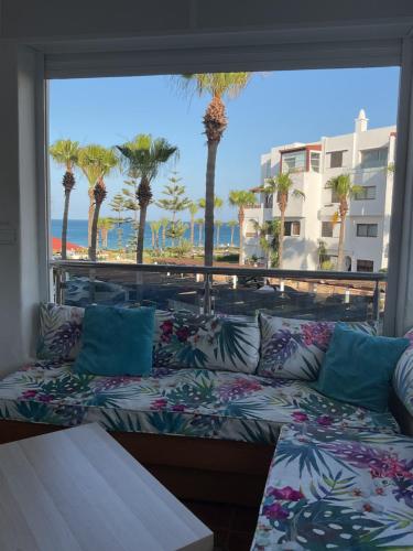 a couch sitting in front of a window with palm trees at Appartement marina beach f5 n6 in M'diq
