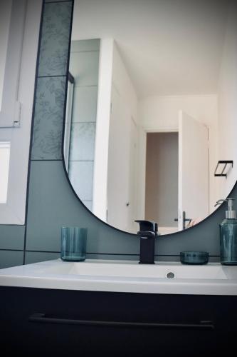 La salle de bains est pourvue d'un grand miroir et d'un lavabo. dans l'établissement Chaleureux appartement avec parking gratuit, à Ifs
