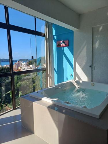a bathroom with a bath tub with a large window at Suíte Atlântica com banheira de hidromassagem in Bombinhas