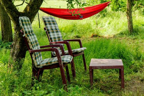two chairs and a stool next to a tree with an umbrella at Träumen unter Bäumen - Omas lütte Obstbutze am See in Lübstorf