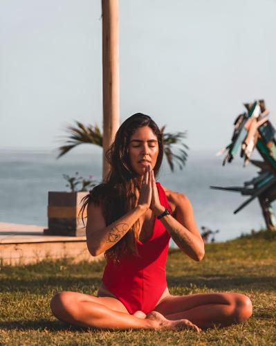 a woman sitting on the grass doing a yoga pose at qema Mancora in Máncora