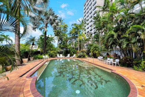 a swimming pool with palm trees and a building at Belle Escapes 101 Rydges Plaza Esplanade with Panoramic Ocean Views in Cairns